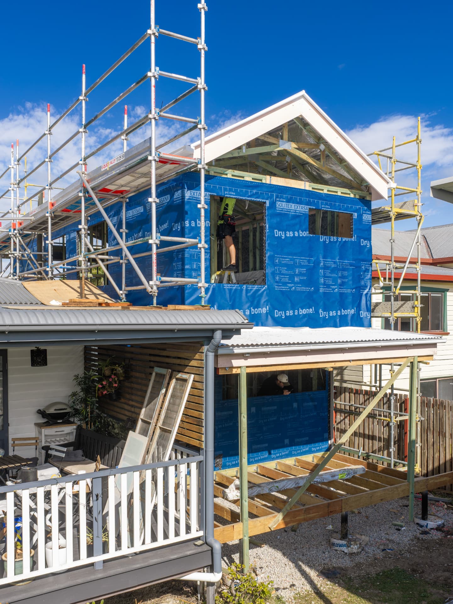 Second-storey home extension under construction in Deagon, Brisbane — scaffolding, timber framing, and blue weather wrap